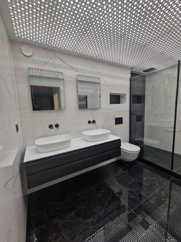 Double vasque sur meuble foncé, plafond acoustique perforé et sol en marbre noir